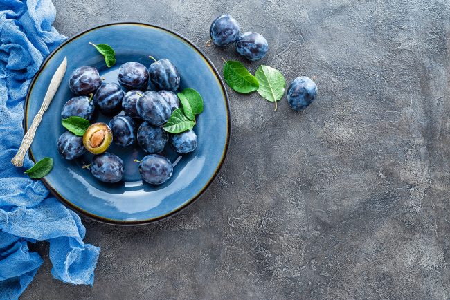 Fresh juicy sweet plums on plate with leaves