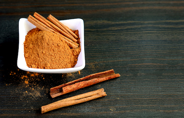 Bowl,Of,Ground,Cinnamon,Powder,With,Cinnamon,Stick,On,Black