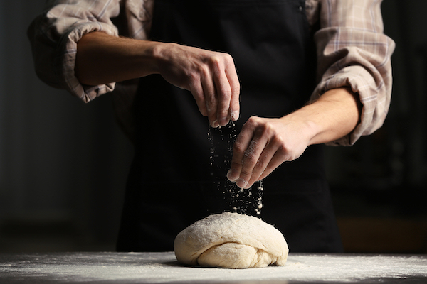 Man,Sprinkling,Flour,Over,Fresh,Dough,On,Kitchen,Table