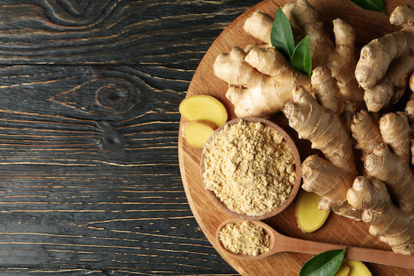 Board with ginger and ginger powder on wooden background