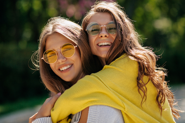 Close-up outside portrait of friendly best friends. Joyful blonde young woman in yellow shirt posing with smile next to laughing friend relaxing outdoor
