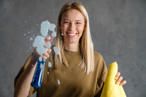 Happy blonde woman maid holding bottle of detergent
