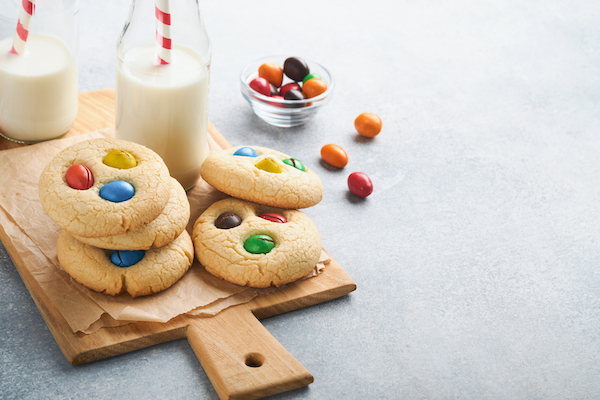Homemade cookies with colorful chocolate candies and milk. Stack of shortbread cookies with multi colored candy on plate with bottle of milk on light gray background. Baby food concept. Copy space.
