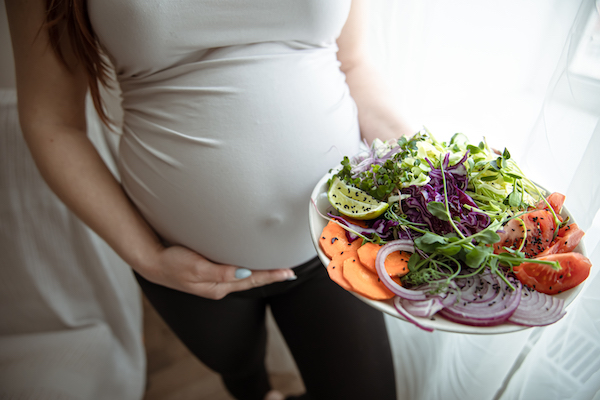 Close-up of a bright salad of fresh vegetables in the hands of a pregnant woman.