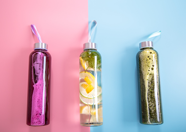 Glass bottles with natural drinks on a colored background .