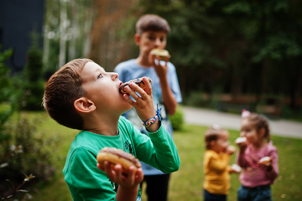 Four kids with doughnuts at evening yard. Tasty yummy donut food.