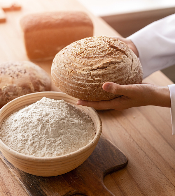 Crop baker carrying bread near flour