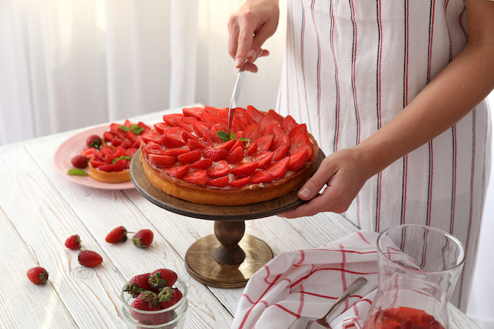 Woman in apron cut the strawberry tart