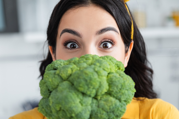brunette woman looking at camera near ripe broccoli