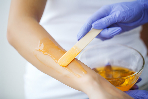 Master does epilation of hands with help of sugar paste hot wax in salon beauty.