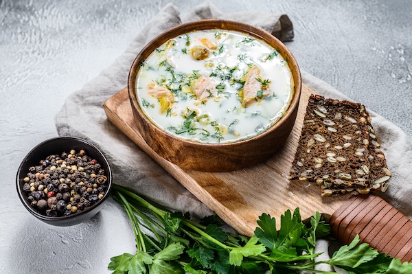 Creamy fish soup with salmon, trout, potatoes and parsley. Gray background, top view.
