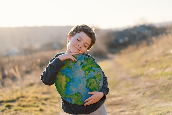Little boy holding planet in hands against green spring background. Earth day