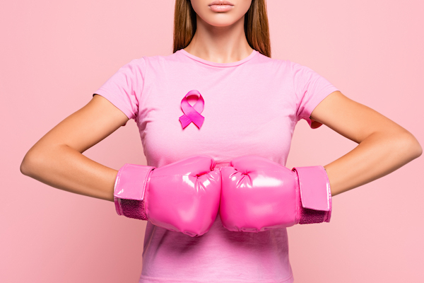 Partial view of woman in boxing gloves wearing sign of breast cancer awareness isolated on pink