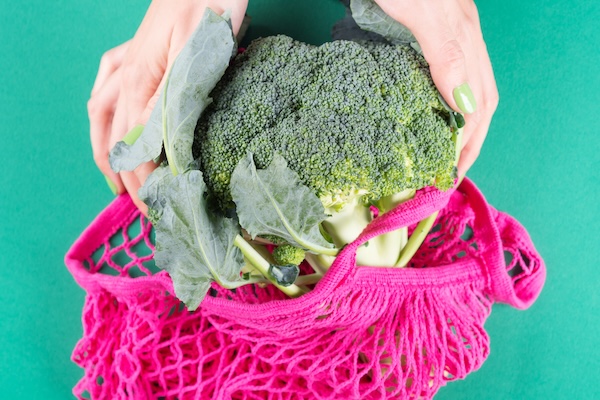 Woman holding pink reusable bag with broccoli