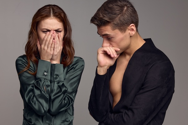 A puzzled man and an upset woman on a gray background are gesturing with their hands