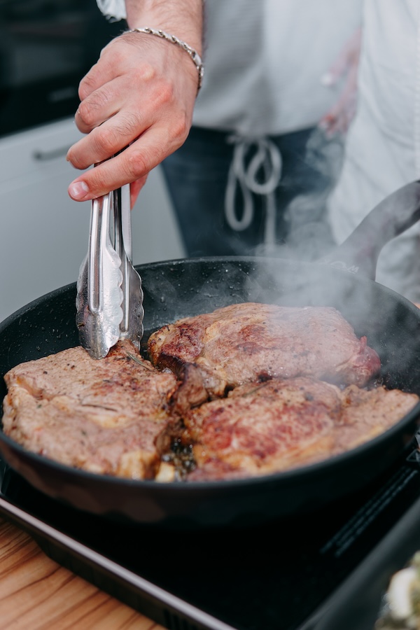 cooking steaks in a pan. cooking beef at the culinary master class. the hands of the chef in black gloves.