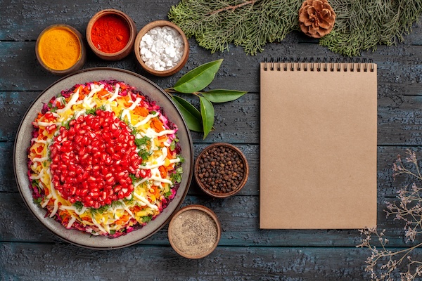 top view tasty food appetizing Christmas food and five bowls of colorful spices next to the cream notebook spruce branches with cones