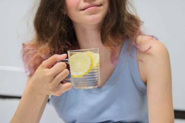 Girl sitting in bed with glass of water with lemon