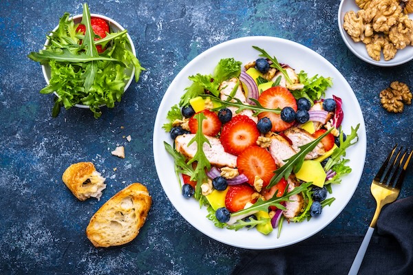 Foodie food salad with strawberry, chicken, arugula, blueberries, avocado and walnuts, blue table., top view
