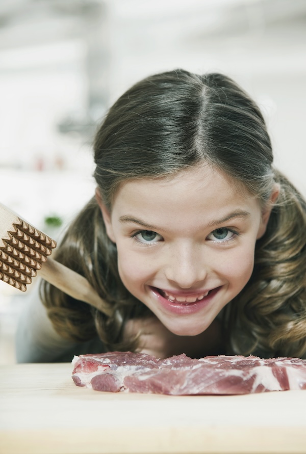 Germany, Cologne, Girl cutting meat using meat tenderiser