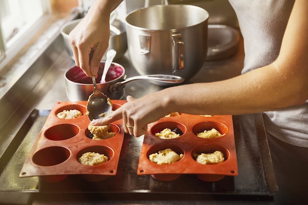 High angle close up person using spoon to place small portions of cake dough into silicone mold.