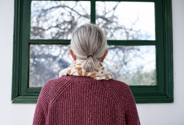 Rear view of senior gray haired woman looking out of the window
