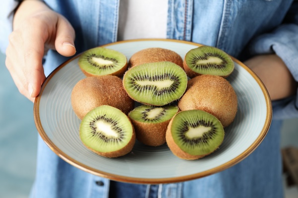 Woman in shirt holding plate of ripe kiwi, close up
