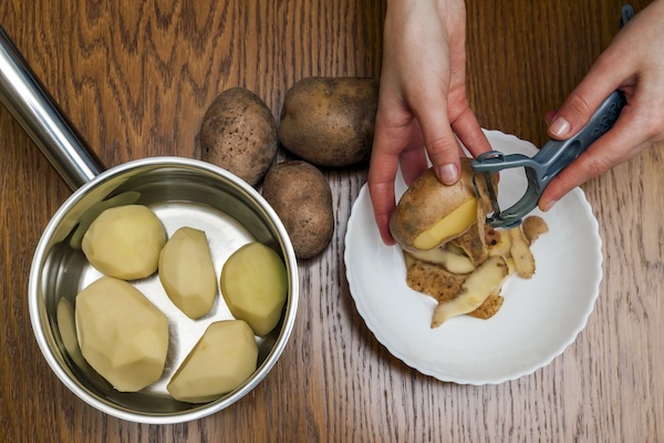 Detail of woman hands peeling fresh yellow potato with kitchen peeler, Food preparation concept.