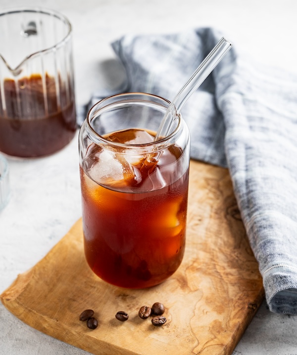 Cold brew coffee in a glass with ice on a wooden board on a light background with coffee beans