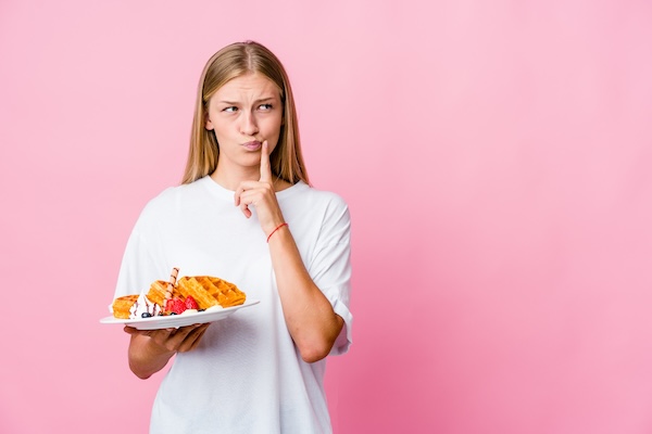 Young russian woman eating a waffle isolated looking sideways with doubtful and skeptical expression.