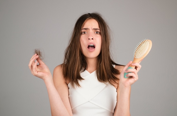 Hair loss. Woman is upset of hair loss. Portrait of sad girl with problem hair, isolated. Worried girl holding long damaged unhealthy hair in hand.
